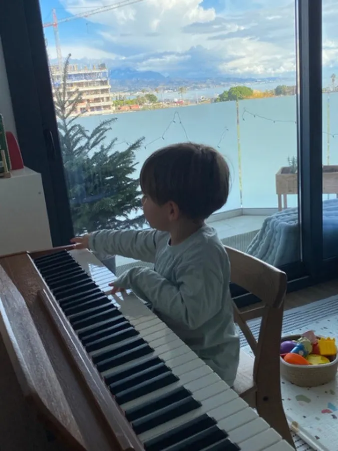 My son playing the piano by a sunny window