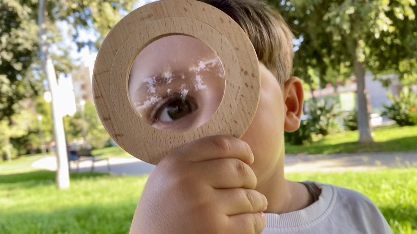 Child looking through a wooden magnifying glass outdoors